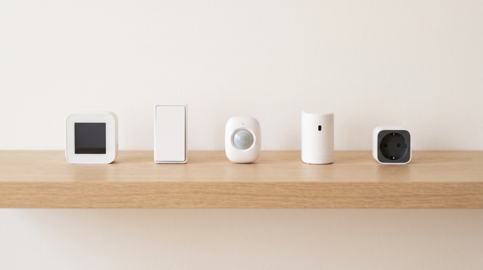 Five unbranded white smart home devices on a pale oak shelf, representing the Aqara vs Sonoff, Shelly and Tuya comparison
